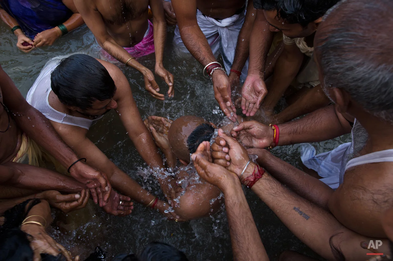 In this Aug. 29, 2015, photo, Hindu devotees bath a sadhu, or Hindu holy man, center, in the Godavari River during Kumbh Mela, or Pitcher Festival in Nashik, India. Hindus believe taking a dip in the waters of a holy river during the festival will cleanse them of their sins. (AP Photo/Tsering Topgyal)