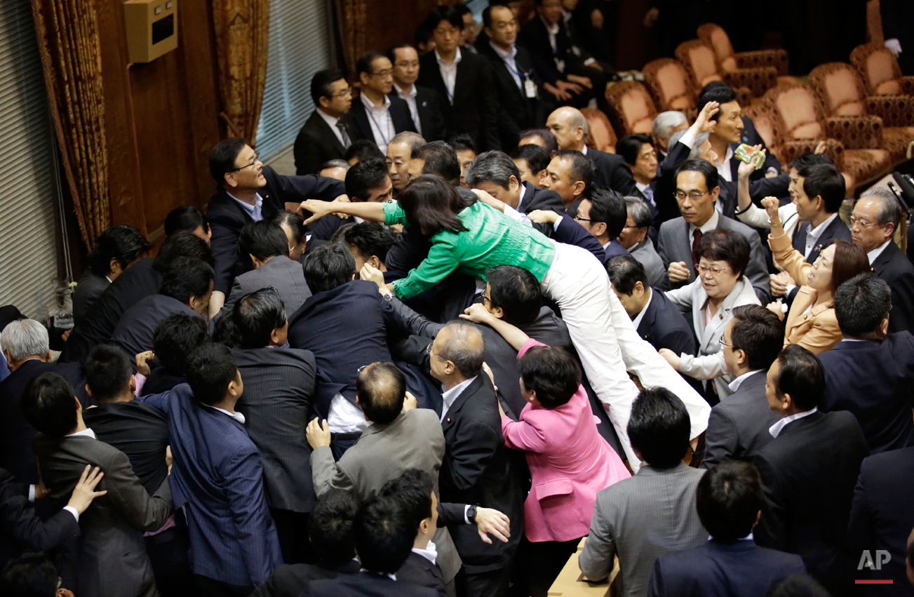  In this Thursday, Sept. 17, 2015 photo, opposition lawmakers surge toward the chairman's seat to protest as ruling party colleagues rush in to try to protect him during a committee voting of security bills at the upper house of the parliament in Tok