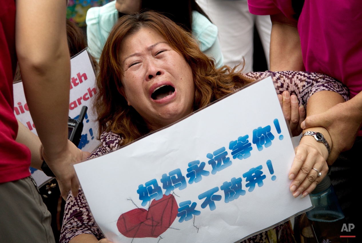  In this Aug. 7, 2015 photo, a relative of a passenger aboard Malaysia Airlines Flight 370 that went missing on March 8, 2014, is carried away by policemen as she and other family members kneel down and cry in front of the media during a protest near