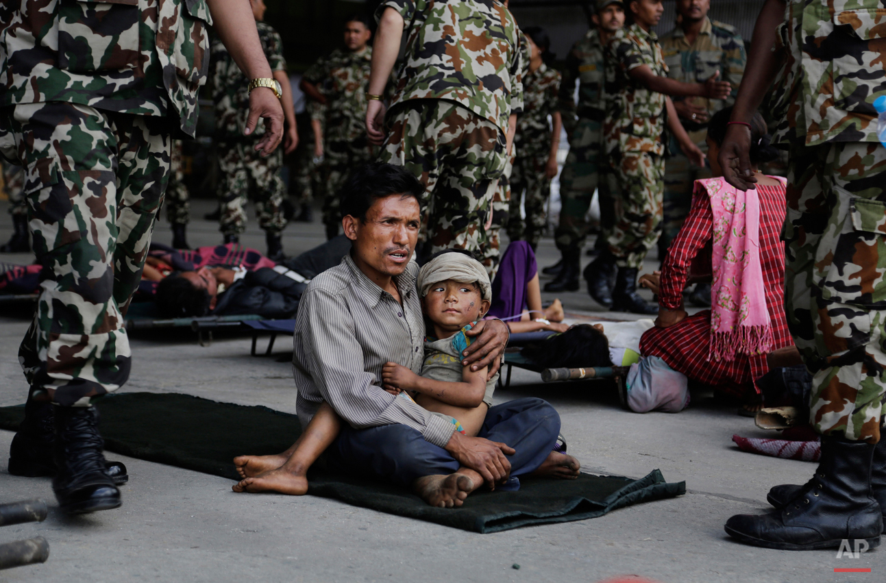  A man sits with a child on his lap as victims of Saturdayís earthquake, wait for ambulances after being evacuated at the airport in Kathmandu, Nepal, Monday, April 27, 2015. The death toll from Nepal's earthquake is expected to rise depended largely