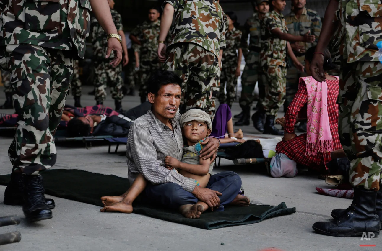A man sits with a child on his lap as victims of Saturdayís earthquake, wait for ambulances after being evacuated at the airport in Kathmandu, Nepal, Monday, April 27, 2015. The death toll from Nepal's earthquake is expected to rise depended largely on the condition of vulnerable mountain villages that rescue workers were still struggling to reach two days after the disaster. (AP Photo/Altaf Qadri)
