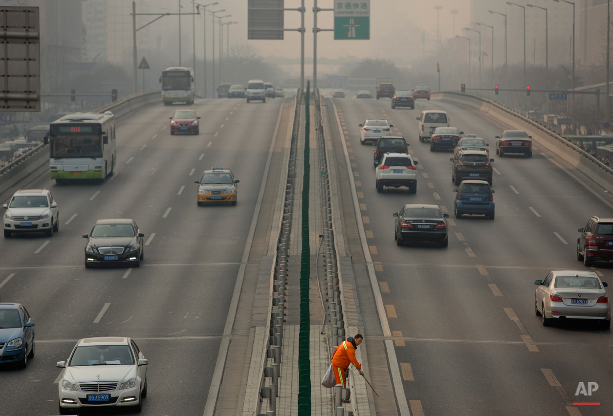  In this March 6, 2015, photo, a road worker picks up trash along the median of a highway on a smoggy day in Beijing. Chen Jining, China's minister of Environmental Protection, held a press conference on Saturday to talk about the country's efforts t