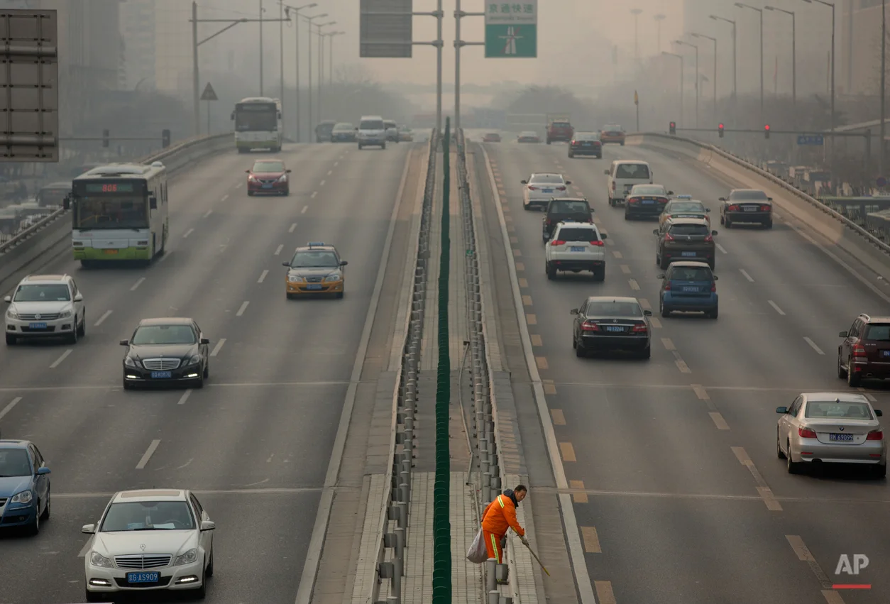 In this March 6, 2015, photo, a road worker picks up trash along the median of a highway on a smoggy day in Beijing. Chen Jining, China's minister of Environmental Protection, held a press conference on Saturday to talk about the country's efforts to fight pollution. (AP Photo/Mark Schiefelbein)