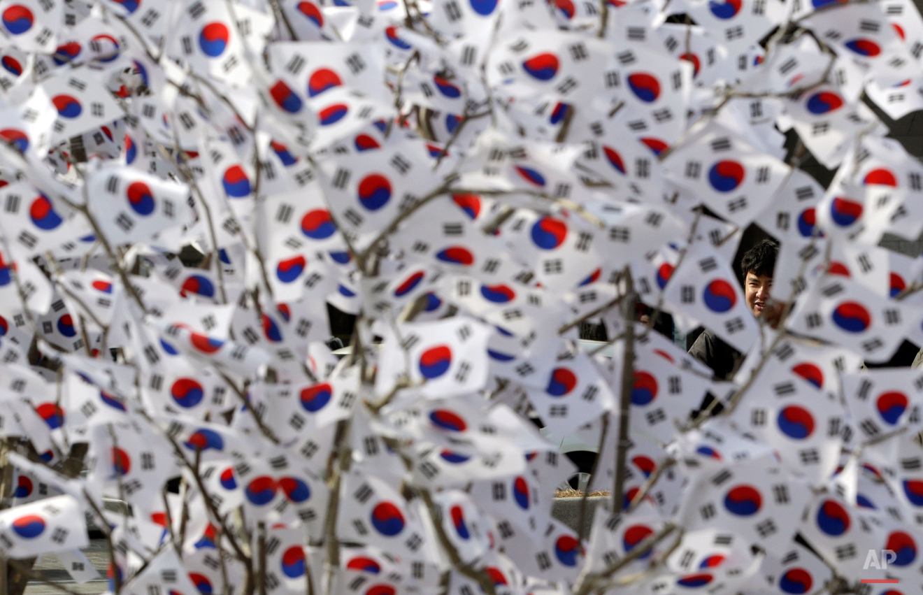  In this Thursday, Feb. 26, 2015, photo, a man looks at South Korean national flags hanging on a tree to celebrate the upcoming March First Independence Movement Day, the anniversary of the 1919 uprising against Japanese colonial rule during a street