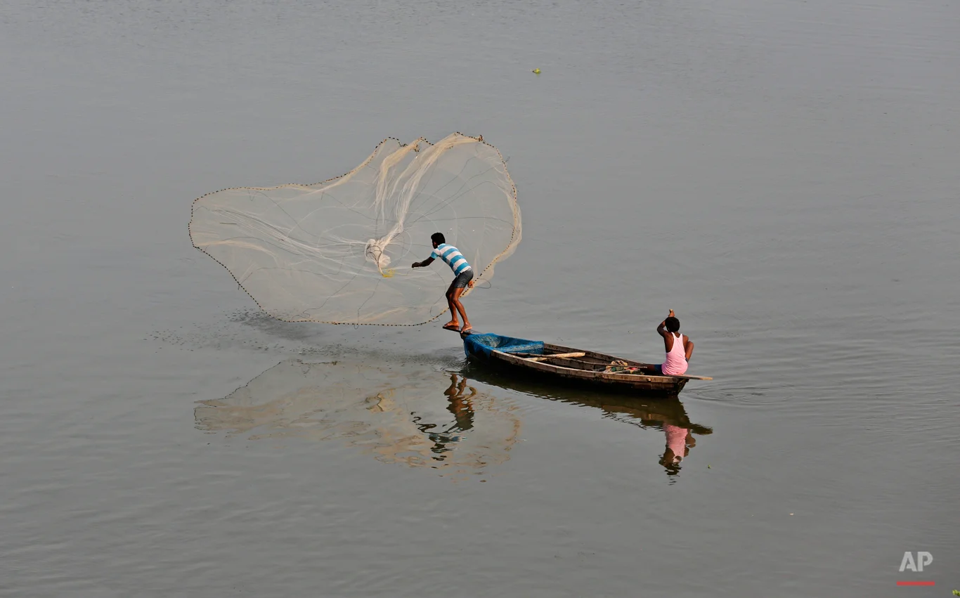 In this Aug. 7, 2015 photo, an Indian fisherman throws a fishing net into the Gomti River in Lucknow, India. It is considered auspicious to take a dip in the waters of the River Gomti so as to rid away the sins, as per the Hindu mythology. (AP Photo/Rajesh Kumar Singh)