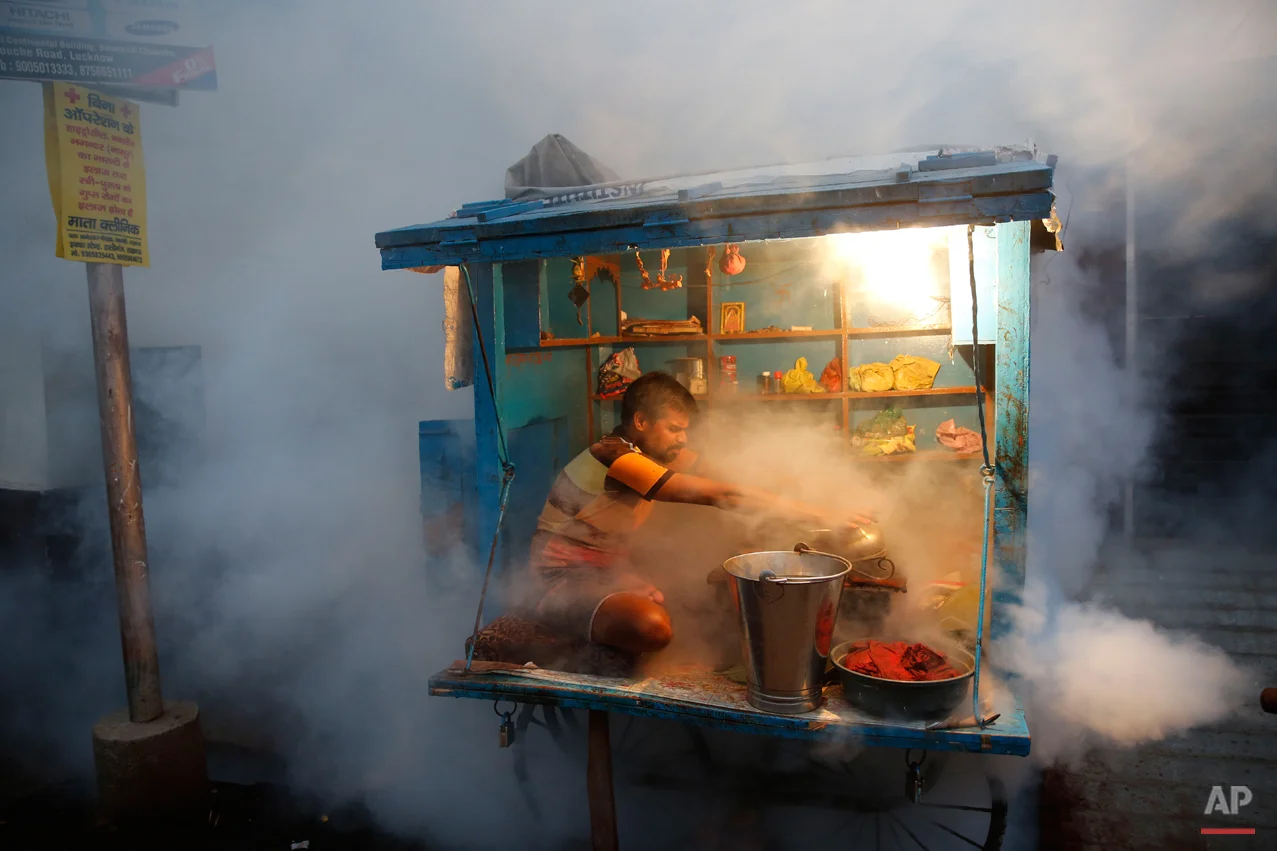 In this Tuesday, Sept. 22, 2015 photo, a man who sells chewable tobacco covers his items as a municipal worker fumigates to prevent mosquitoes from breeding in Lucknow, India. Dengue outbreaks are reported every year after the monsoon season that runs from June to September. Many people have died from the mosquito-borne disease in the country???s capital New Delhi this year. (AP Photo/Rajesh Kumar Singh)