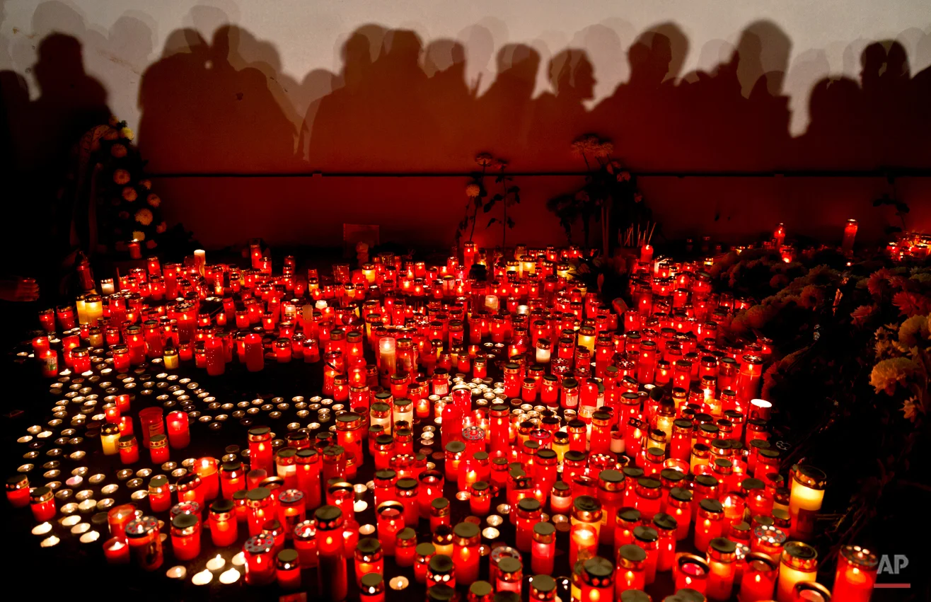  People cast shadows on a wall as they wait to light candles and lay flowers outside the compound that housed the nightclub where a fire occurred in the early morning hours in Bucharest, Romania, Saturday, Oct. 31, 2015. Hundreds of young people had 