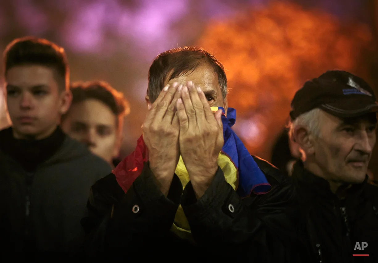  A man with a Romanian flag wrapped around his neck holds his palms in front of his face during the fourth day of protests, joined by tens of thousands across the country, calling for early elections, in Bucharest, Romania, Friday, Nov. 6, 2015. Larg