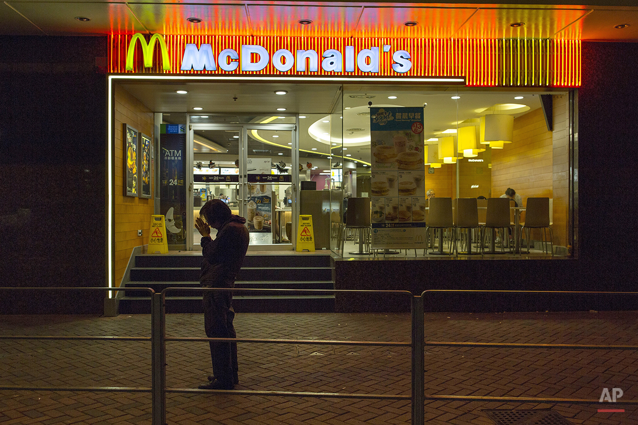  In this Oct. 30, 2015 photo, a man, who has been sleeping at night in a 24-hour McDonald’s branch in Hong Kong, prays outside the restaurant.in Hong Kong. The recent death of a woman at a Hong Kong McDonald’s, where her body lay slumped at a table f