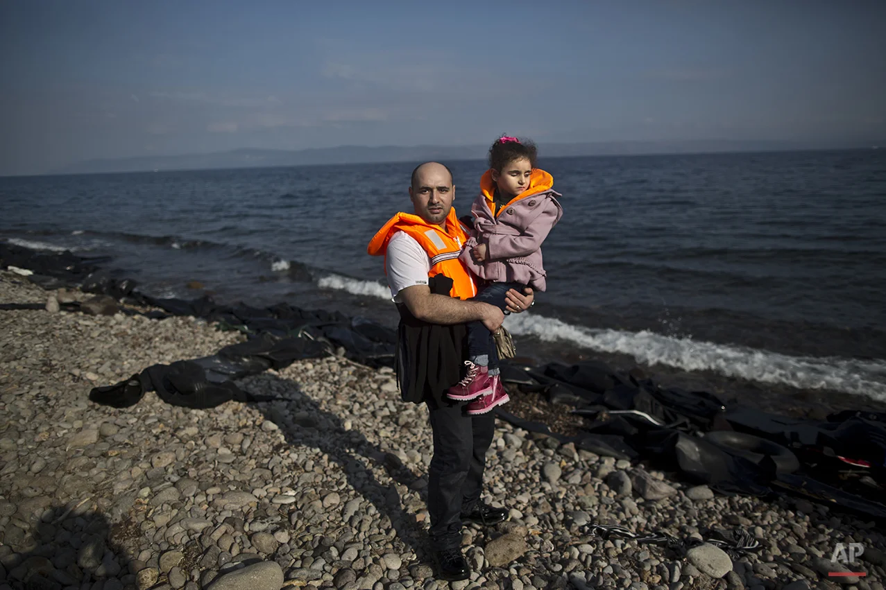 In this photo taken on Saturday, Oct. 3, 2015, Syrian refugee Mahmoud Naoura, 30, who came from Aleppo, Syria, poses for a picture while holding his daughter Huda, 5, who was injured in 2012 by a government bombing on their home which made her lose her sight, shortly after arriving on a dinghy from the Turkish coast to the northeastern Greek island of Lesbos. Naoura said “I just want to cure my daughter. Huda will see again, inshallah, and when she will open her eyes I want her to see a safe environment around.” (AP Photo/Muhammed Muheisen)