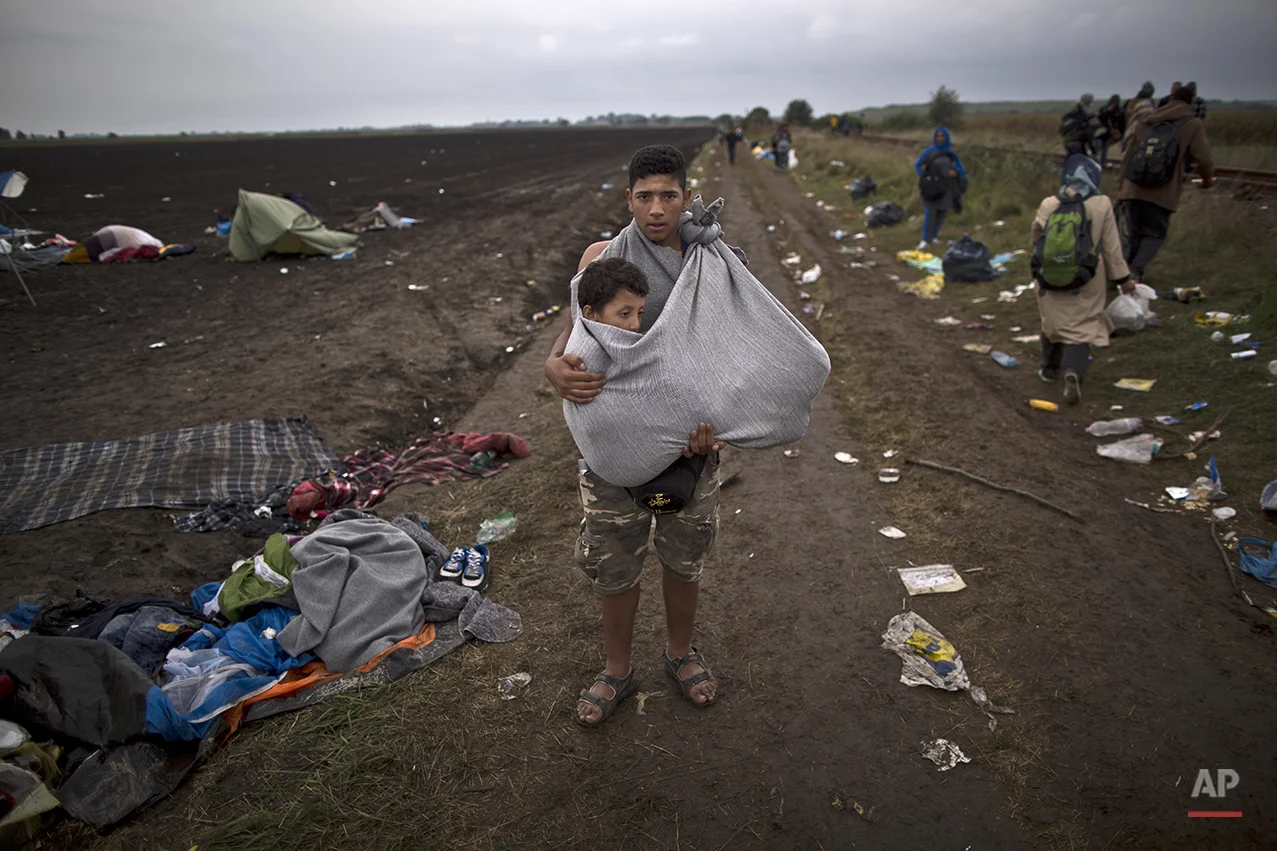 In this photo taken on Friday, Sept. 11, 2015, Syrian refugee Hussein Sbaih, 18, who came from Damascus, Syria, carries his cousin Saifuallah, 7, whose legs are broken, while posing for a picture after they crossed the Serbian-Hungarian border near Roszke, southern Hungary. "My cousin's legs are broken and I had to carry him for long distances I am so tired and lost and have no clue where we are going,” Sbaih said. (AP Photo/Muhammed Muheisen)