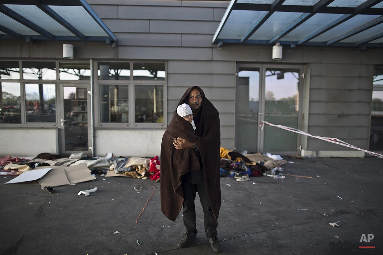 In this photo taken on Wednesday, Sept. 23, 2015, Syrian refugee Jamal Almasri, 54, who came from Damascus, Syria, wraps himself and his granddaughter with a shawl to shelter from the morning cold as he poses for a picture, after spending the night at a collection point in the truck parking lot of the former border station on the Austrian side of the Hungarian-Austrian border near Nickelsdorf, Austria. Almasri said, "We met death, we just want to have a life, any life with a rooftop and a shelter. Our lives are over, what matters is the children.” (AP Photo/Muhammed Muheisen)