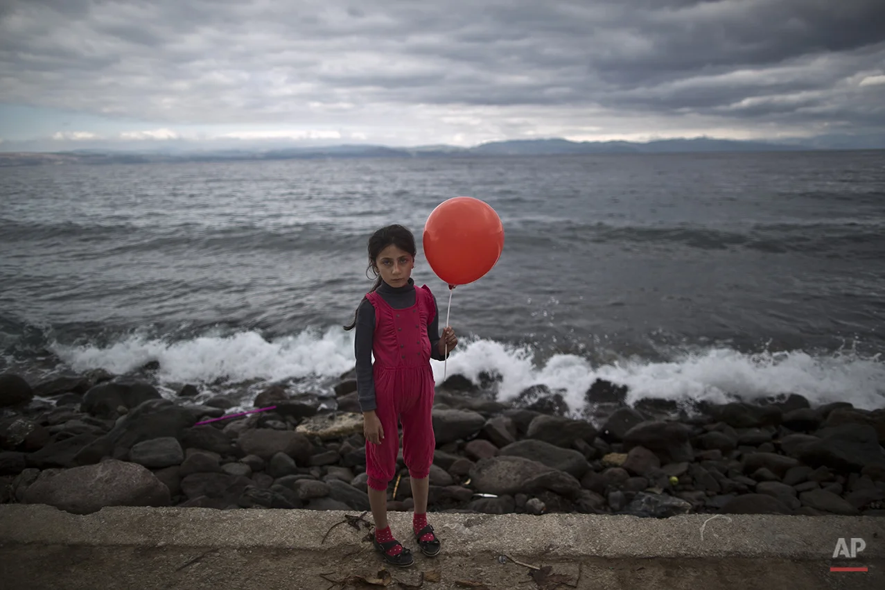 In this photo taken on Friday, Oct. 2, 2015, Syrian refugee Raghad Faleh, 8, who came with her family from Idlib, Syria, poses for a picture while holding a balloon given to her by volunteers, a few hours after she and her family arrived on a dinghy from the Turkish coast to the northeastern Greek island of Lesbos. “My feet are killing me from pain, I walked a lot,” Faleh said. (AP Photo/Muhammed Muheisen)