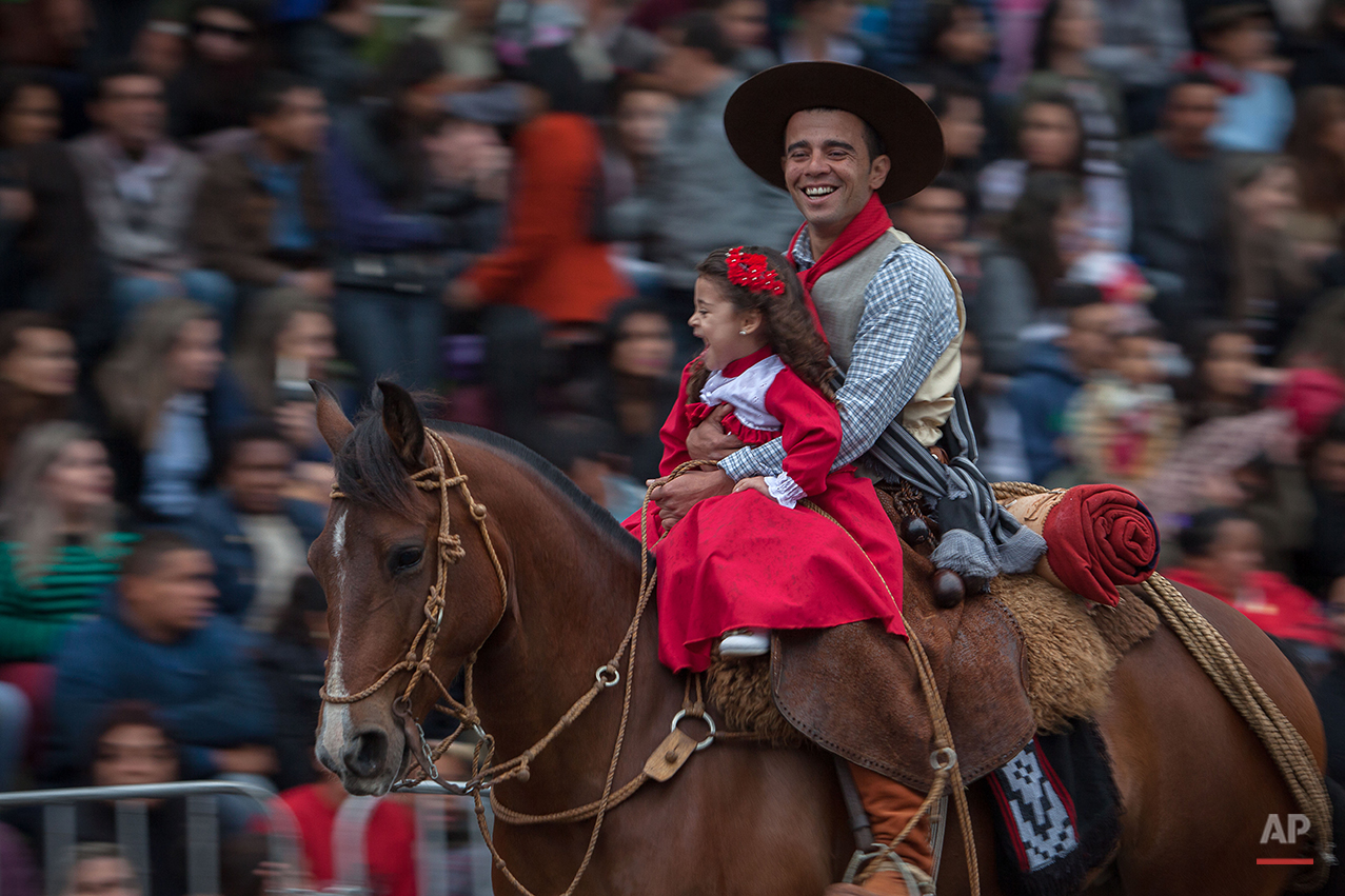  In this Sept. 20, 2015 photo, a father with his daughter smile during a parade at the Semana Farroupilha or “Ragamuffin” week, in Alegrete municipality, Rio Grande do Sul state, Brazil. Some of the Brazilian cowboys ride with little girls wearing ol