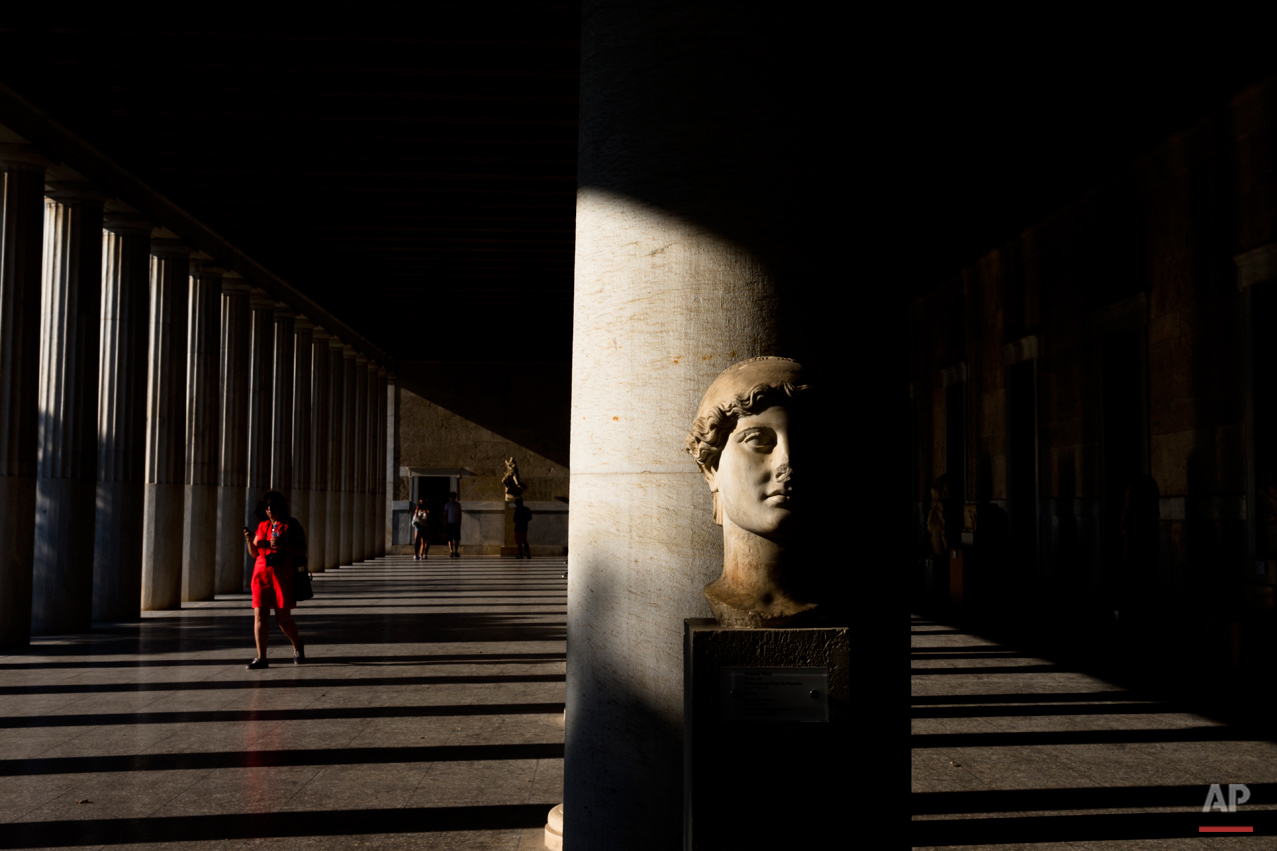A woman walks behind a 2nd century A.D. marble head of victory inside Stoa of Attalos, at ancient agora, in Athens, Sunday, Aug. 30, 2015. (AP Photo/Petros Giannakouris)