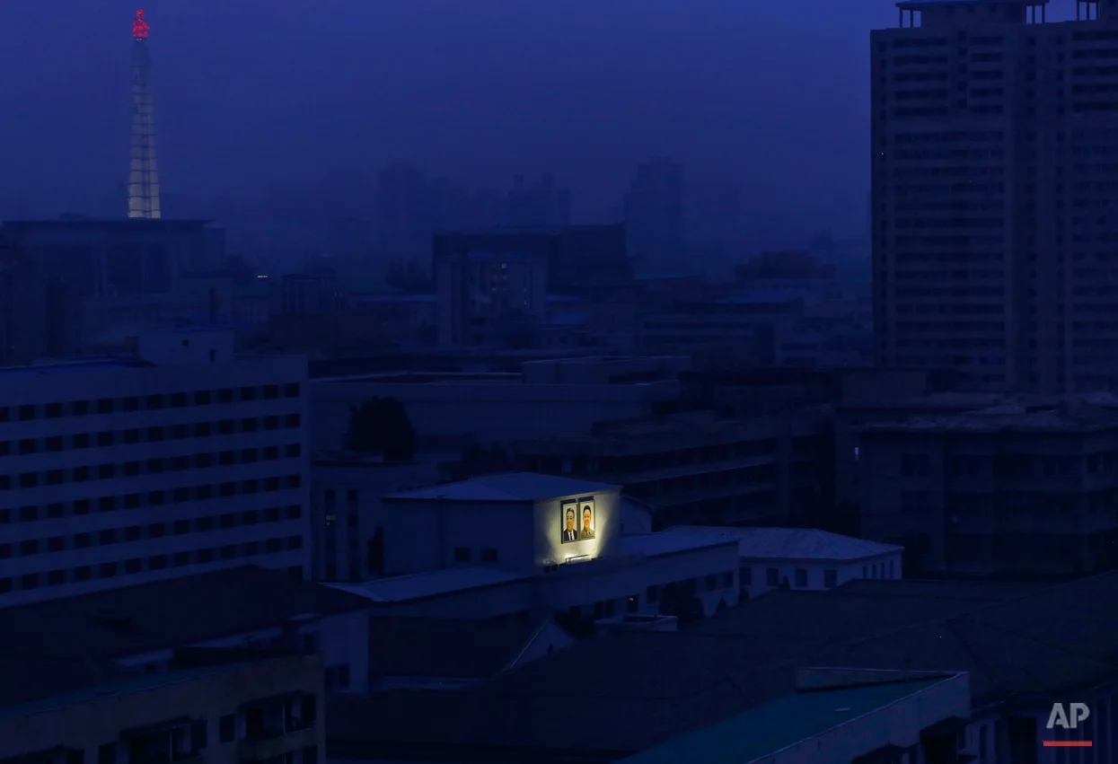 Portaits of the late North Korean leaders Kim Il Sung, left, and Kim Jong Il glow on the facade of a building as the Juche Tower, top left, one of the city's landmarks, is seen in the background at dawn in Pyongyang, North Korea, Wednesday, Aug. 19, 2015. (AP Photo/Dita Alangkara)