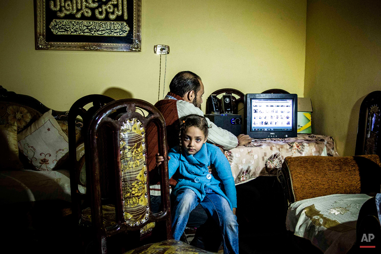  In this picture taken on Dec. 19, 2014, Jana Amr Elbana, a 5-year-old girl whose father was shot to death during a pro-Muslim Brotherhood protest in 2014, sits with her uncle Sameh Elbana who is showing her photos of her father, at their home in Bad