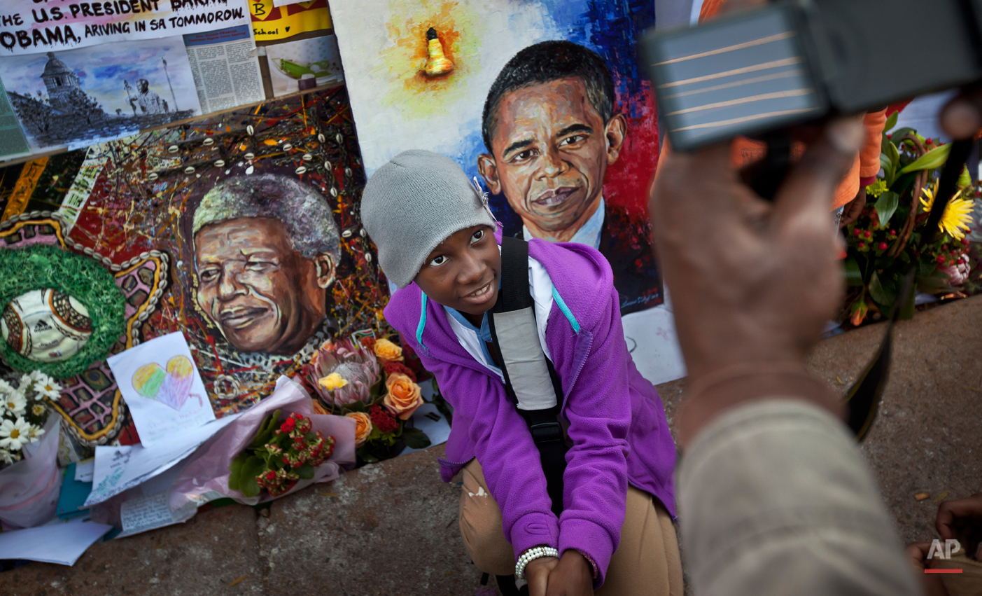  In this Saturday June 29, 2013 photo, children squat to have their photograph taken by their parents next to paintings of President Barack Obama, center, and former South African President Nelson Mandela, left, outside the Mediclinic Heart Hospital 