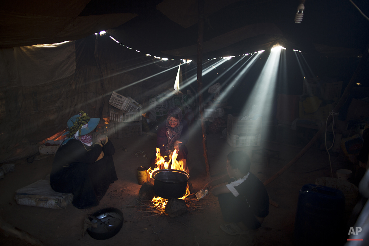  In this Sunday, July 26, 2015 photo, a Syrian refugee girl sits with her mother while cooking on a fire inside their tent at an informal tented settlement near the Syrian border on the outskirts of Mafraq, Jordan. Most of those in Mafraq choose to l