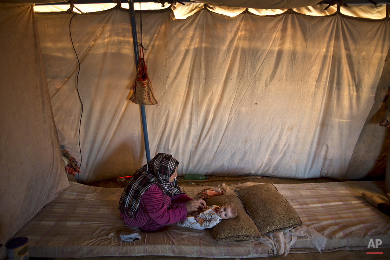  In this Tuesday, July 21, 2015 photo, Syrian refugee Naela Mohammed, 31, changes the clothes of her daughter Asmahan, 4 months, at their tent in an informal tented settlement near the Syrian border on the outskirts of Mafraq, Jordan. Naela worries a