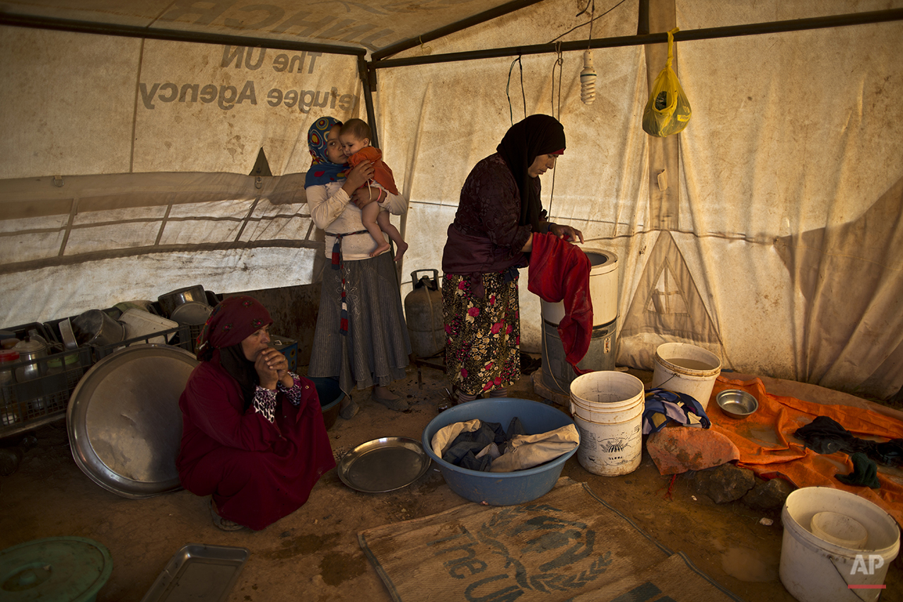  In this Wednesday, July 22, 2015 photo, a Syrian refugee girl holds her younger sister while her mother, right, washes clothes inside their tent at an informal settlement near the Syrian border on the outskirts of Mafraq, Jordan. Aid agencies asked 