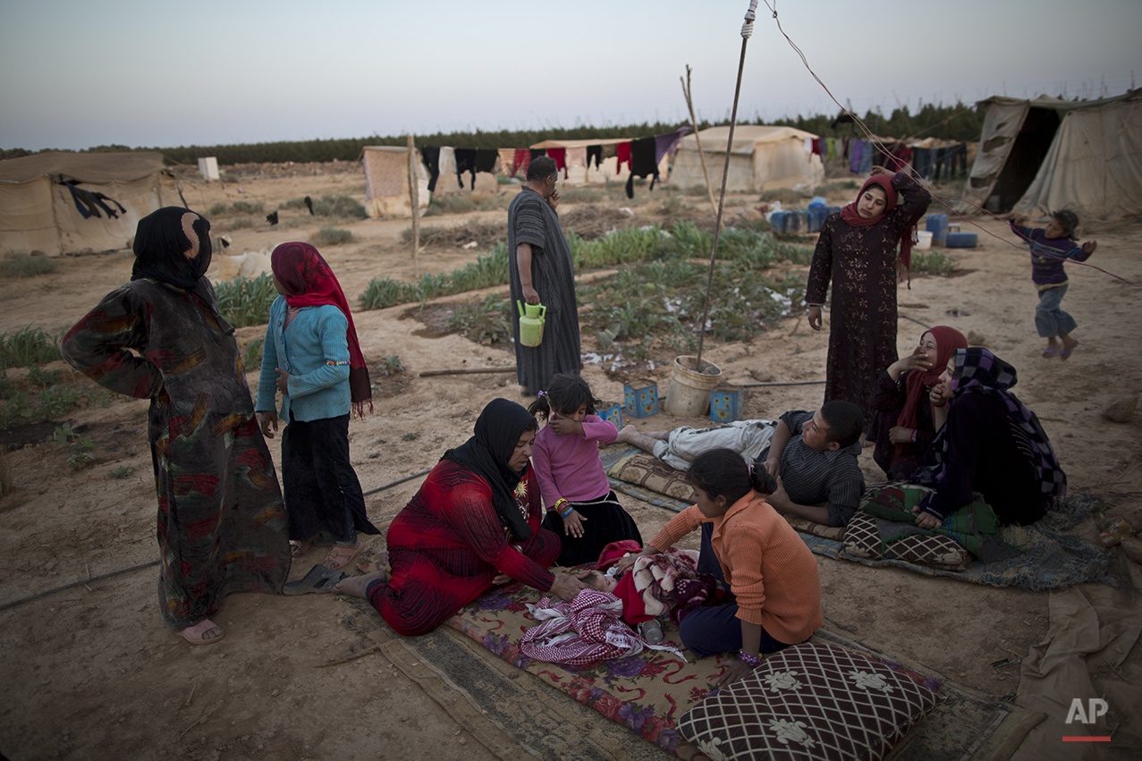  In this Sunday, July 26, 2015 photo, a Syrian refugee woman sits on the ground next to her infant suffering from a high temperature due to an infection in her throat, outside their tent at an informal settlement near the Syrian border on the outskir