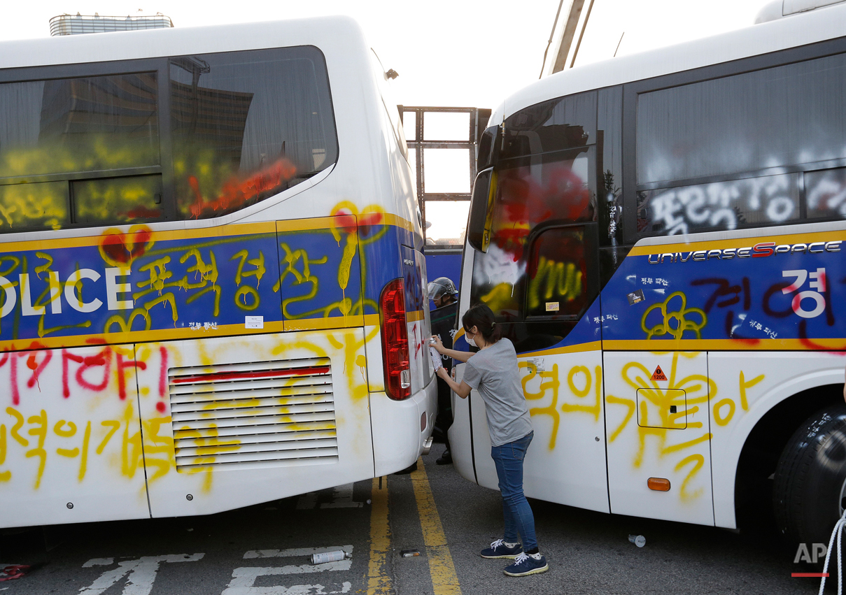  A member of the Korean Confederation of Trade Unions sprays paints to write a message denouncing South Korean President Park Geun-hye on police buses after a May Day rally in Seoul, South Korea, Friday, May 1, 2015. Thousands of South Koreans marche