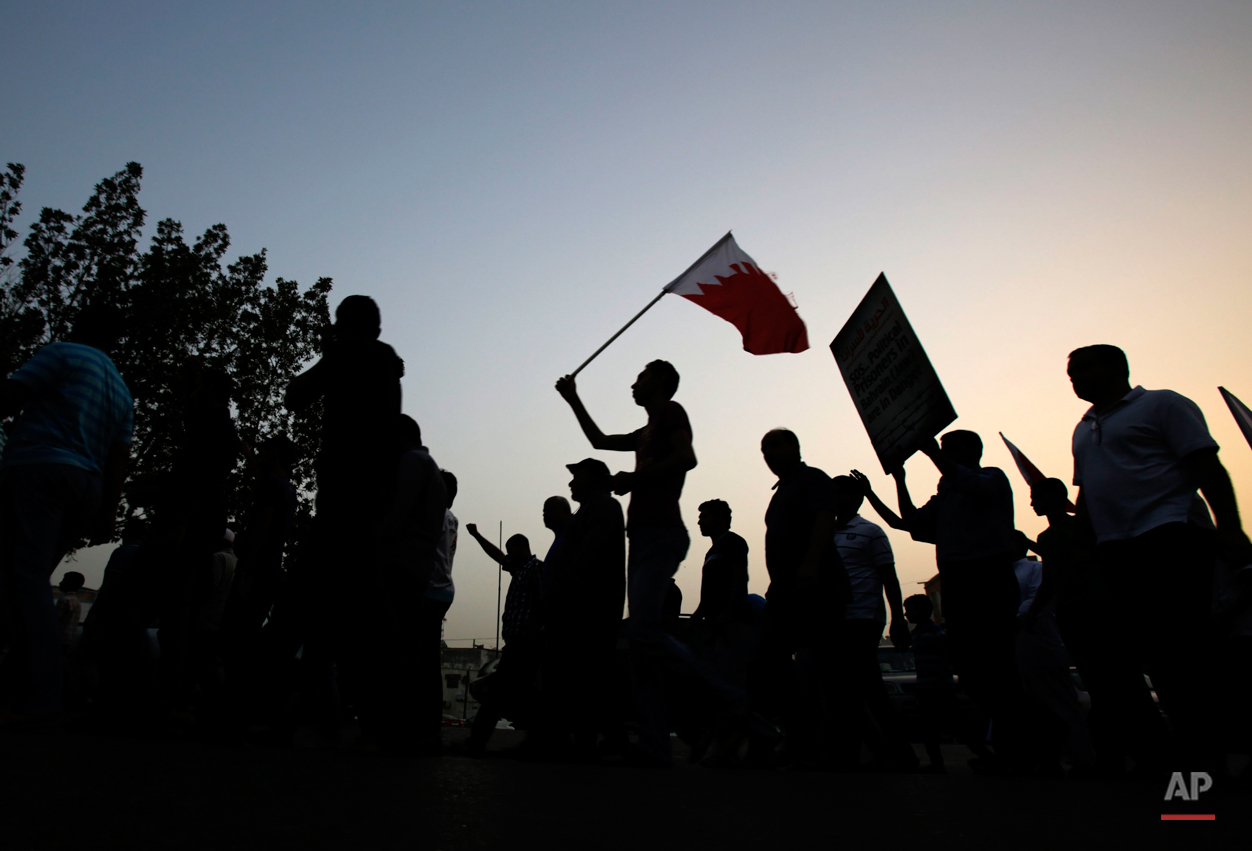  A small group of Bahraini men, carrying national flags and signs supporting political prisoners, march quickly between police patrols, on the lookout for violators of a protest ban, in Manama, Bahrain, Friday, May 1, 2015. The government denied perm