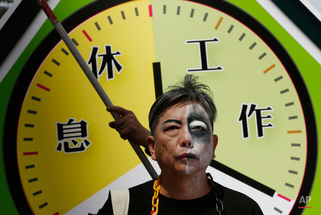  A protester with half of his face painted as zombie in front of a mock clock divided into "rest," left, and "work," right, during a march to mark May Day in Hong Kong Friday, May 1, 2015. Hundreds of protesters from various labor unions staged a ral