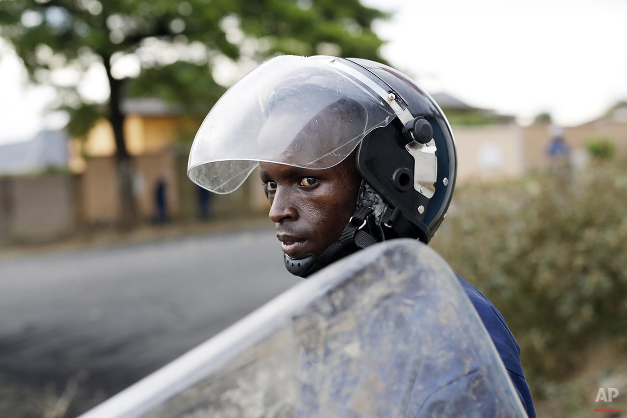  A Burundi riot police officer watches a group of stone throwing demonstrators during clashes in the Musaga district of Bujumbura, Burundi, Tuesday April 28, 2015. Anti-government street demonstrations continued for a third day after six people died 