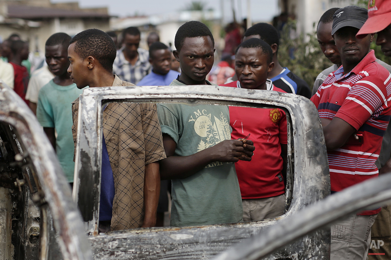  Residents of the Musaga neighborhood stand by the burnt out remains of a car in Bujumbura, Burundi, Friday May 1, 2015. Anti-government street demonstrations continued for a sixth day after in protests against the move by President Pierre Nkurunziza