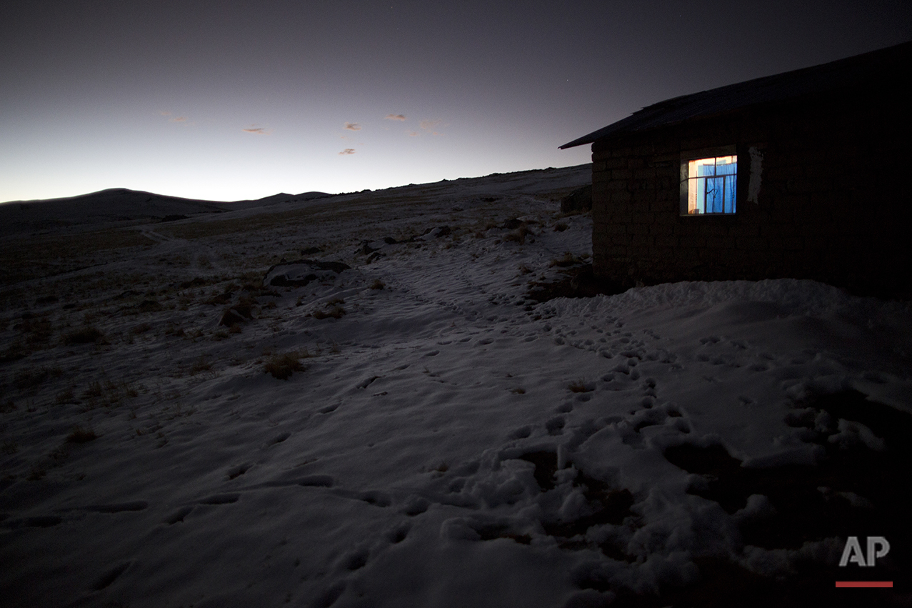  In this July 9, 2016 photo, light shines from a home's window in the late afternoon amid fields of snow in San Antonio de Putina in the Puno region of Peru, an area where locals raise alpaca and sheep for their wool. Every winter freeze destroys the