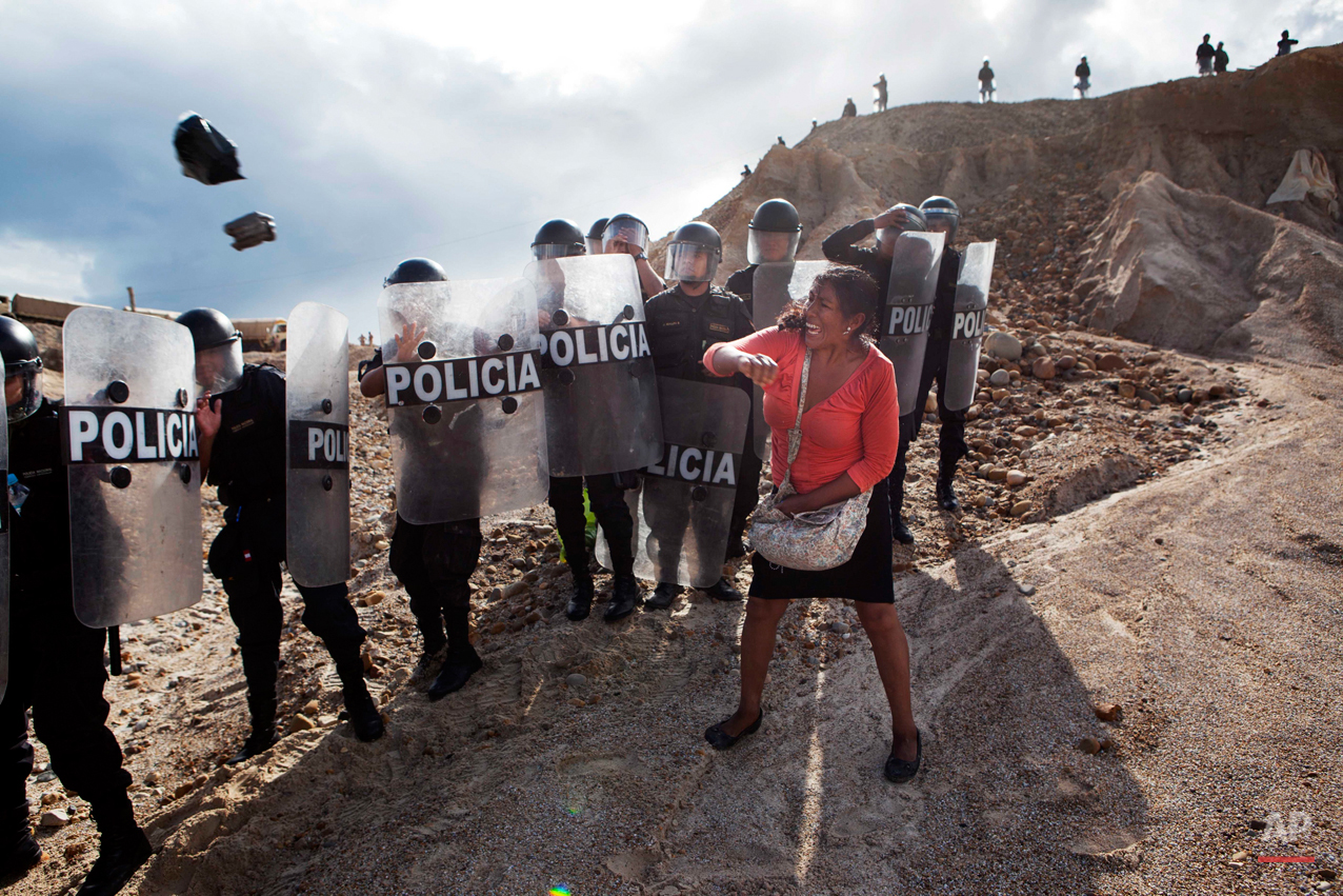 A new threat now looms for the estimated 20,000 wildcat miners who toil in a huge scar of denuded rainforest known as La Pampa, an area nearly three times the size of Washington, D.C. Peru's government declared all informal mining illegal on April 19, 2014, and began a crackdown.
A woman throws a rock and a bag at riot policemen who block her way home in Huepetuhe district in Peru's Madre de Dios region in Peru, Monday, April 28, 2014. Soldiers, police and marines have begun destroying illegal gold mining machinery in Peru’s southeastern jungle region of Madre de Dios, enforcing a ban on illegal mining in the Huepetuhe district. Before the deadline, miners clashed with police while intermittently blocking traffic on the Interoceanic Highway that links the Pacific with Brazil. (AP Photo/Rodrigo Abd)