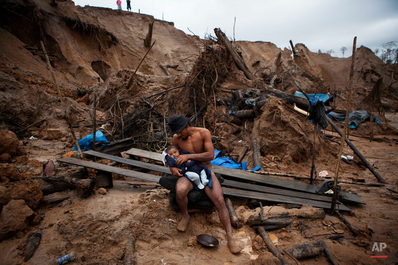 Manuel Espinosa holds his four-month-old son, Edward, brought to him by his wife as he takes a break from mining gold in La Pampa, Peru in the Madre de Dios region on Friday, May 2, 2014. Madre de Dios state has an estimated 40,000 illegal miners, most centered near the commercially vital Interoceanic Highway that links the Pacific Ocean with Brazil. (AP Photo/Rodrigo Abd)