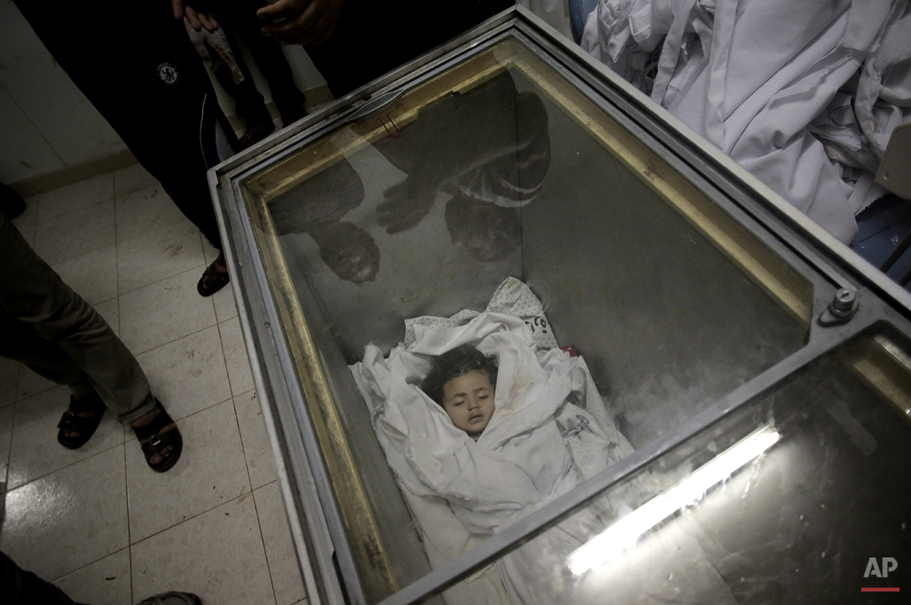  Palestinians gather around the lifeless body of Raghad Masoud, 34 months, who was killed in an Israeli strike, after she was laid in a freezer as the hospital morgue was full at Rafah refugee camp, in southern Gaza Strip, Monday, Aug. 4, 2014.  Isra