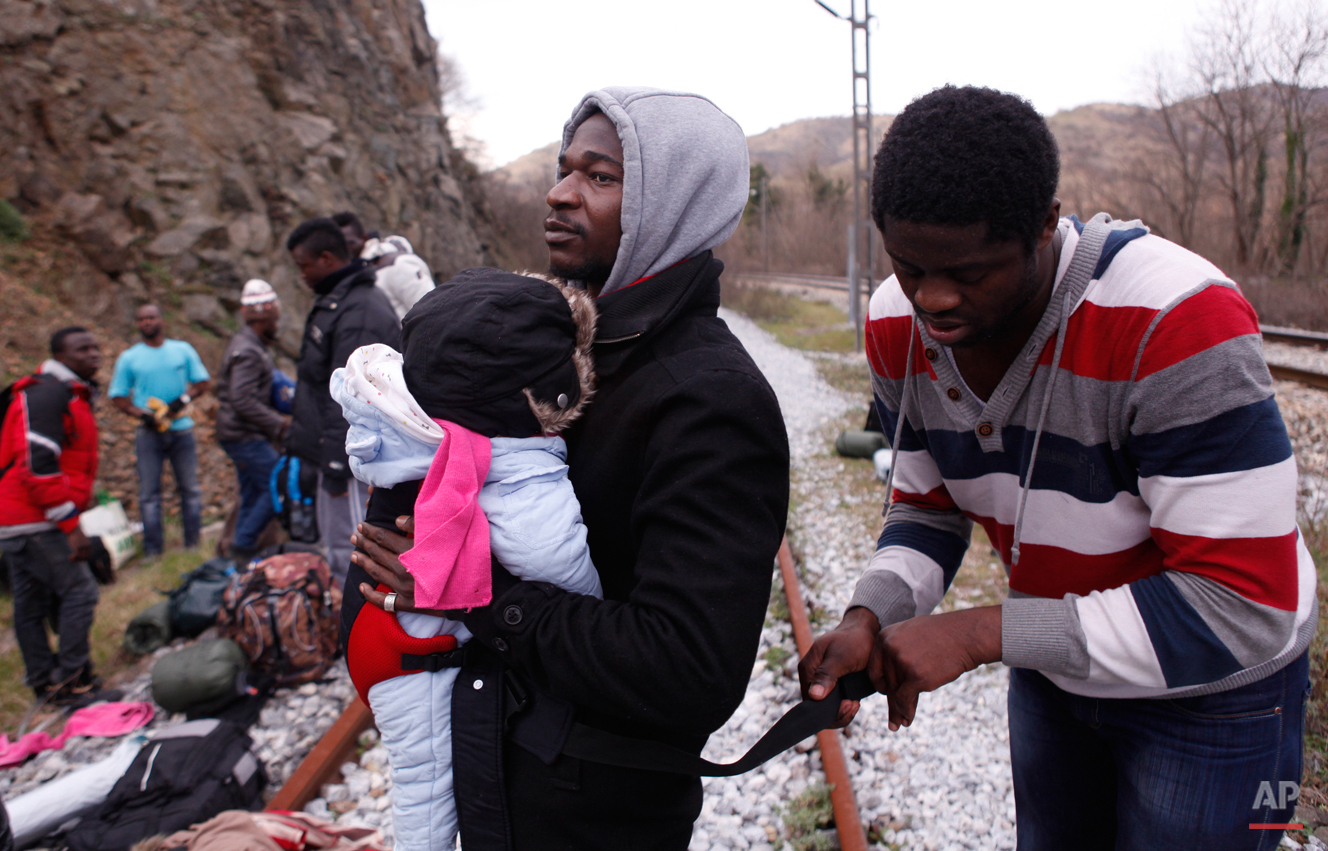  In this Saturday, Feb. 28, 2015 photo Jean-Paul Apetey of Ivory Coast receives help from Francis Tchiaze of Cameroon as he helps to carry ten-months-old Christian on their way to the town of Evzonoi, Greece.  The tide of hopeful migrants pours throu
