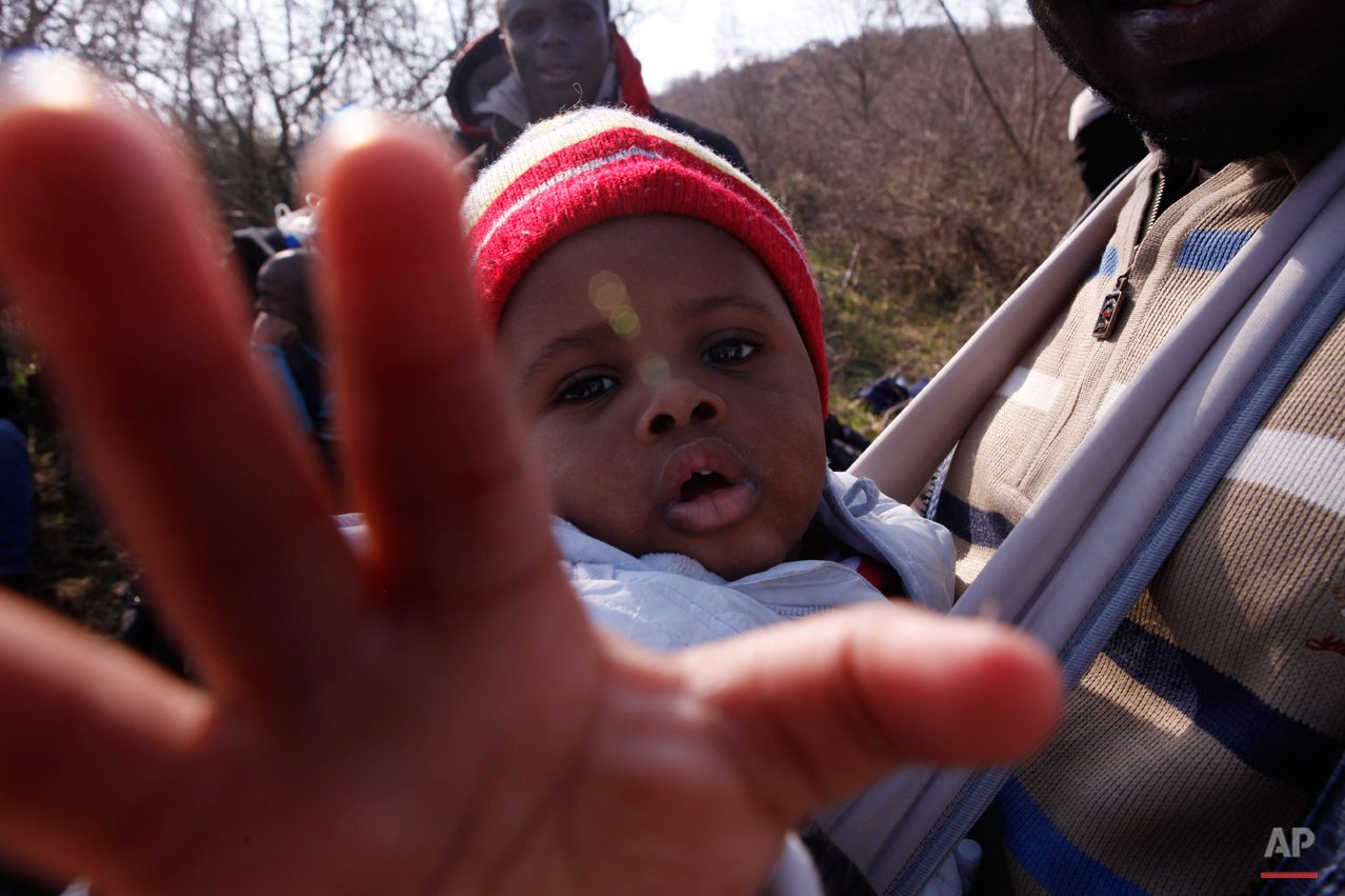  In this Saturday, Feb. 28, 2015 photo 10-months-old migrant Christian Djeukam reaches out to the lens of the photographer as he sits in a baby carrier near the town of Evzonoi, Greece. The tide of hopeful migrants pours through the vulnerable 'back-