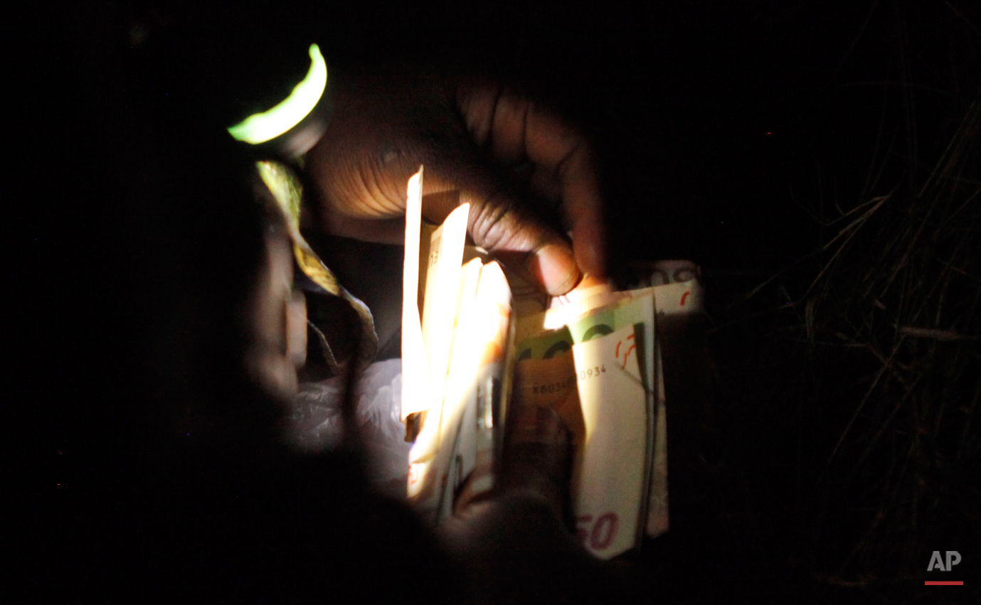  In this Thursday, March 5, 2015 photo a woman holds a flashlight in her mouth as she counts her savings near Nogotino, Macedonia.  The tide of hopeful migrants pours through the vulnerable 'back-door' countries in the hope of entering the 28-nation 