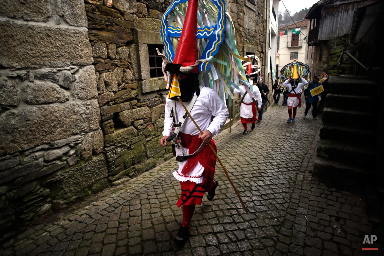 In this photo taken on Saturday, Feb. 14, 2015 revellers dressed in Carnival traditional costumes dance and jump as they parade during Carnival festivities in Lazarim, northeastern Portugal. While Rio de Janeiro may boast the worldís most famous carnival, the festive period of masquerades and wild and colorful costumes that precedes the Christian religious season of Lent is also a permanent and popular fixture for celebration in Spain and Portugal, with each country having its own strange and unique way of doing it. Portugalís most famous carnival takes place in the north-central town of Lazarin, with its pagan ëcaretoí ritual of masked young men dressed in colored woolen quilts and donning brass, leather or wooden masks as they dance and chase local people _ especially young women _ through the streets, trying to scare them by making lots of noise and jingling bells on their backs. (AP Photo/Francisco Seco)