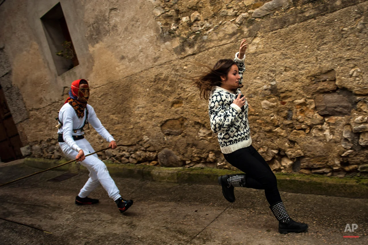 In this photo taken on Sunday, Feb. 15, 2015 a girl runs away from a ''Mamuxarro'' during the carnival, in the small town of Unanu, northern Spain. While Rio de Janeiro may boast the worldís most famous carnival, the festive period of masquerades and wild and colorful costumes that precedes the Christian religious season of Lent is also a permanent and popular fixture for celebration in Spain and Portugal, with each country having its own strange and unique way of doing it. In the northern Spanish ancient village of Unamu, people dress up as 'Mamuxarroí, folkloric figures in white with a red sash and a metal mask to cover their faces as they pursue townsfolk with sticks. According to custom, their 'victims' (usually young women) must kneel and kiss the mamuxarroís knee after he makes the sign of the cross on their forehead. (AP Photo/Alvaro Barrientos)