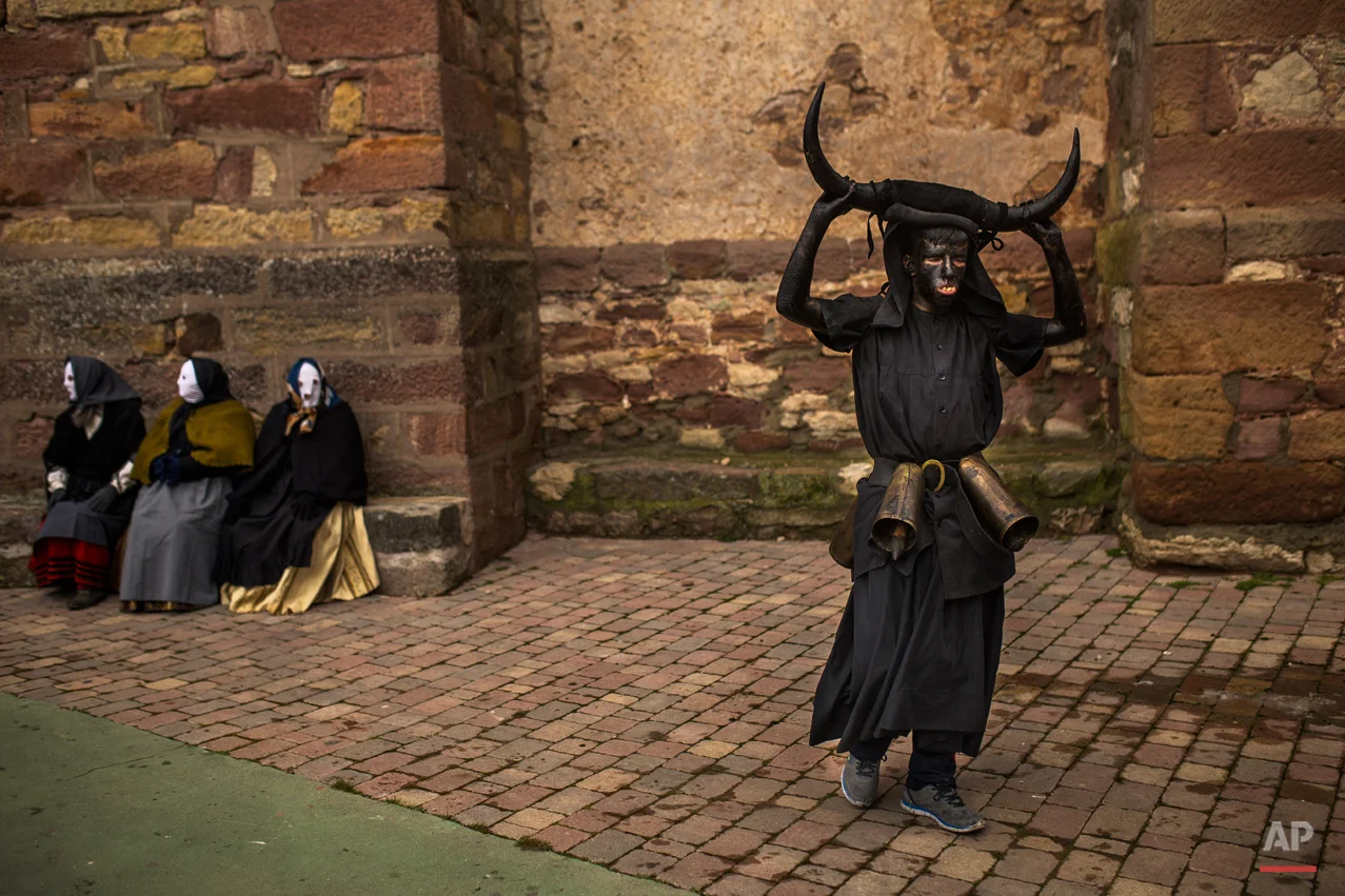 In this photo taken on Saturday, Feb. 14, 2015 a man, covered in oil and soot carrying bull horns on his head and cowbells on a belt representing the devil, walks away from people wearing costumes during a traditional carnival celebration in the small village of Luzon, Spain. While Rio de Janeiro may boast the worldís most famous carnival, the festive period of masquerades and wild and colorful costumes that precedes the Christian religious season of Lent is also a permanent and popular fixture for celebration in Spain and Portugal, with each country having its own strange and unique way of doing it. In Spainís central town of Luzon, men covered in oil and soot wear bull horns and cowbells to represent the devil. Records of Luzonís carnival date as far back as the 14th century although it is believed to be much older. (AP Photo/Andres Kudacki)
