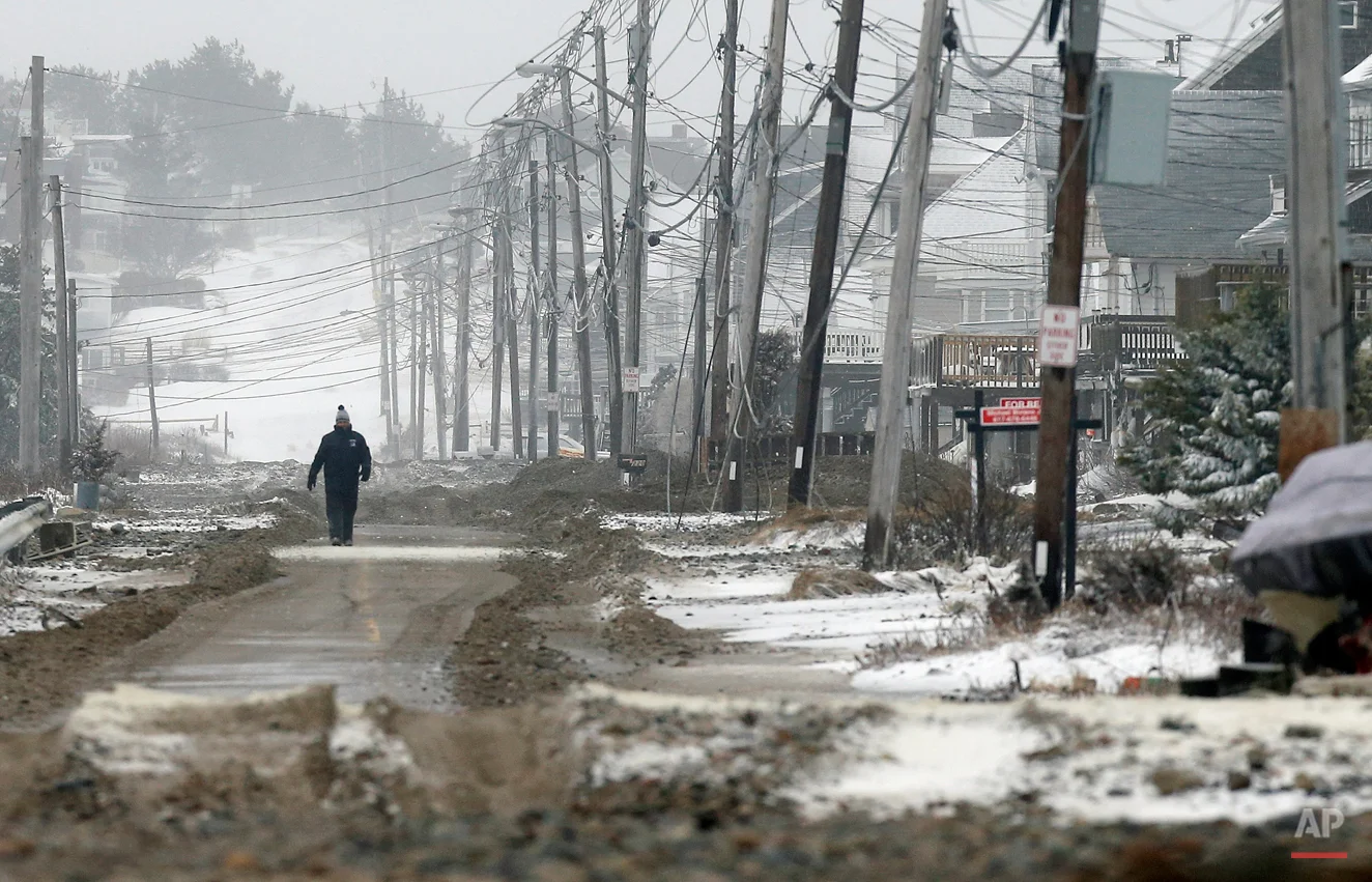 A man walks on a portion of road cleared of sand washed up by ocean waves during a winter storm in the Humarock section of Scituate, Mass., Tuesday, Jan. 27, 2015. (AP Photo/Michael Dwyer)