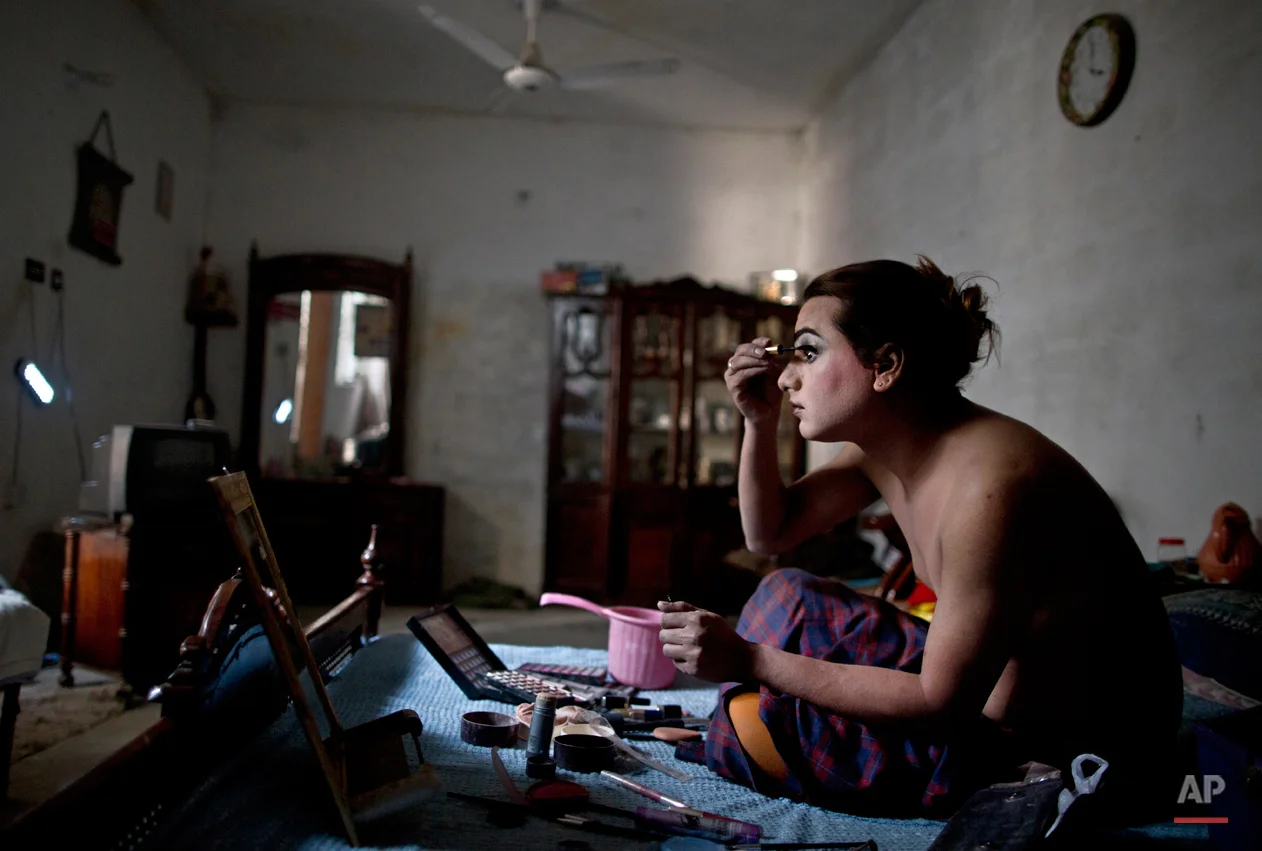In this Saturday, Jan. 10, 2015 photo, Pakistani Waseem Akram, 27, applies makeup on his face using natural light due to a power cut, as he prepares himself for a party at a friend's place in Rawalpindi, Pakistan. By day, Akram sells mobile phone accessories from an alleyway shop in an old neighborhood of this Pakistani city. But by night, Akram stands before a mirror, shaving away his beard and picking through mascara and rouge to become Rani, a female wedding party dancer. (AP Photo/Muhammed Muheisen)