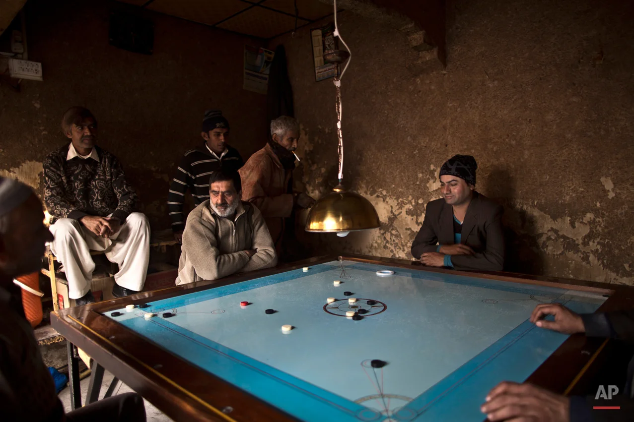 In this Sunday, Jan. 11, 2015, photo, Pakistani Waseem Akram, 27, center, plays a game with neighboring workers at a market in Rawalpindi, Pakistan. By day, Akram sells mobile phone accessories from an alleyway shop in an old neighborhood of this Pakistani city. But by night, Akram stands before a mirror, shaving away his beard and picking through mascara and rouge to become Rani, a female wedding party dancer (AP Photo/Muhammed Muheisen)