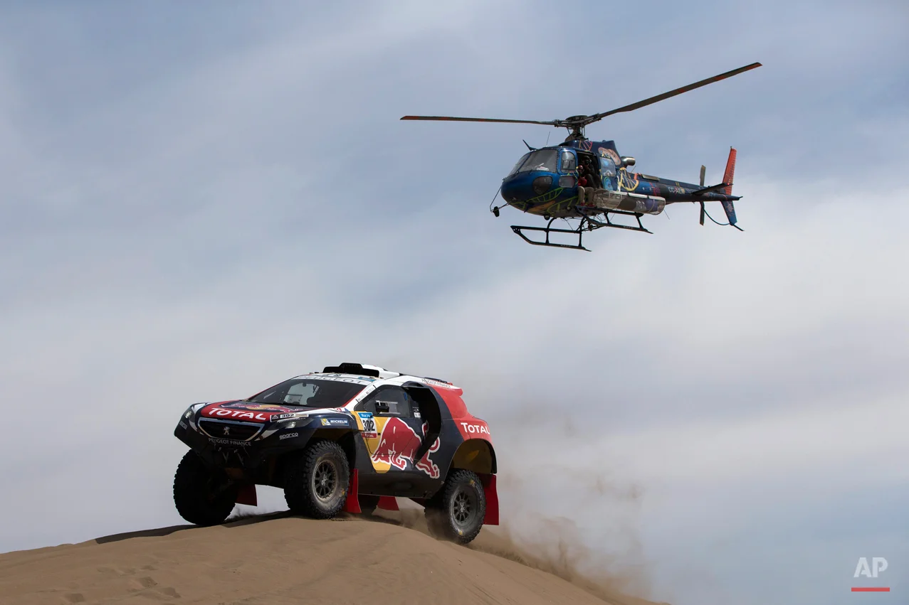 A Dakar helicopter flies over Peugeot driver Stephane Peterhansel and co-pilot Jean Paul Cottret, both of France, as they race through the dunes during the ninth stage of the Dakar Rally 2015 between the cities of Iquique and Calama, Chile, Tuesday, Jan. 13, 2015. The race will finish on Jan. 17, passing through Bolivia and Chile before returning to Argentina where it started. (AP Photo/Felipe Dana)