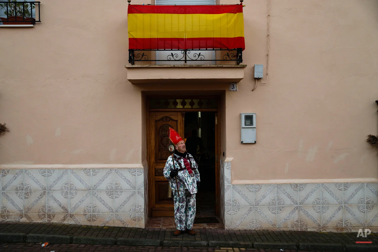 Aniceto Rodrigo, 78, Diablo Mayor or 'greater devil', checks the weather as he leaves his home before walking around the village during the 'Endiablada' traditional festival in Almonacid Del Marquesado, Spain, Tuesday, Feb. 3, 2015. The "Endiablada" (The Brotherhood of the Devils) festivals are celebrated each Feb. 2-3 in the central Spanish town of Almonacid del Marquesado since medieval times or before. In the festival, men from the town dress up as devil-type characters in colorful jumpsuit costumes and red miter hats. They don large heavy copper cowbells around their waists, which clang incessantly as they walk, dance and jump through the town's winding streets and visit the cemetery. The Feb. 3 day procession commemorates the day of Saint Blas. According to a local legend, town shepherds found a statue of the saint and then won a competition with folk from a nearby town to keep the effigy and rang the bells of their animals in celebration. (AP Photo/Daniel Ochoa de Olza)