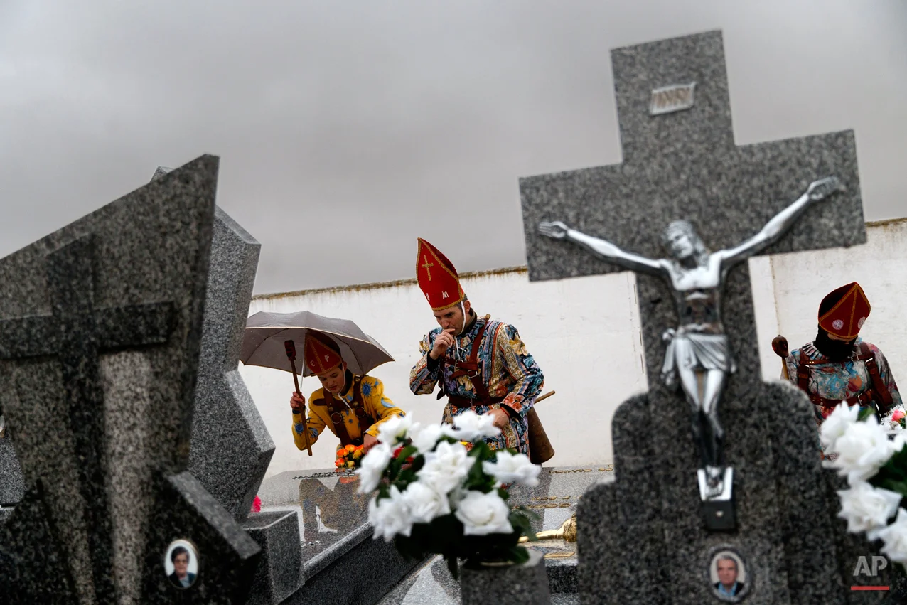 In this Feb. 2, 2015 picture, members of the Endiablada brotherhood pray for the deceased fellow believers and relatives during the 'Endiablada' traditional festival in Almonacid Del Marquesado, Spain. The "Endiablada" (The Brotherhood of the Devils) festivals are celebrated each Feb. 2-3 in the central Spanish town of Almonacid del Marquesado since medieval times or before. In the festival, men from the town dress up as devil-type characters in colorful jumpsuit costumes and red miter hats. They don large heavy copper cowbells around their waists, which clang incessantly as they walk, dance and jump through the town's winding streets and visit the cemetery. The Feb. 2 procession, the "Candelaria" (Candlemas), represents the Virgin Mary presenting baby Jesus to authorities in the temple 40 days after Christmas. The protocol is believed to have caused her some embarrassment and the accompanying bell-clanging characters are thought to be a way of diverting the publicís attention. (AP Photo/Daniel Ochoa de Olza)