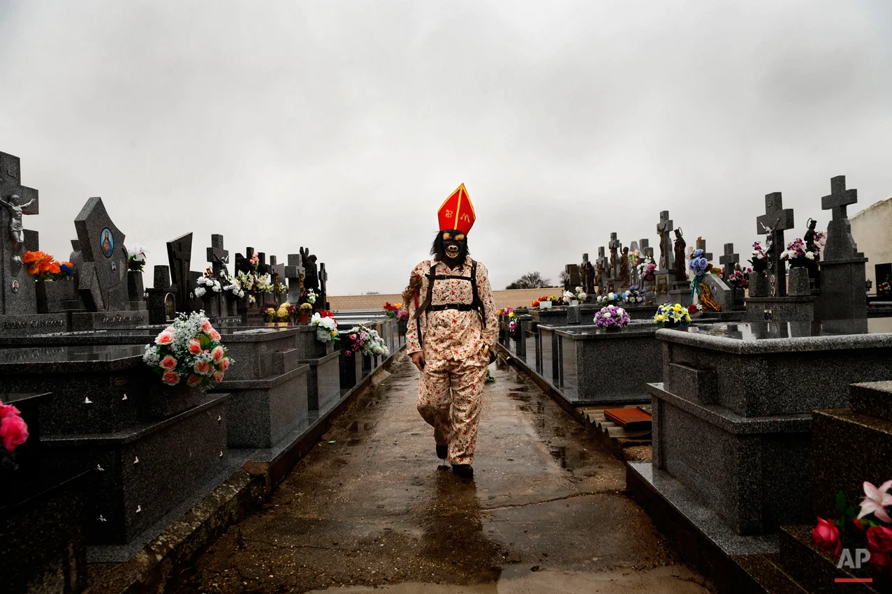 In this Feb. 2, 2015 picture, a member of the Endiablada brotherhood walks trough the cemetery after paying respect to their deceased fellow believers and relatives during the 'Endiablada' traditional festival in Almonacid Del Marquesado, Spain. The "Endiablada" (The Brotherhood of the Devils) festivals are celebrated each Feb. 2-3 in the central Spanish town of Almonacid del Marquesado since medieval times or before. In the festival, men from the town dress up as devil-type characters in colorful jumpsuit costumes and red miter hats. They don large heavy copper cowbells around their waists, which clang incessantly as they walk, dance and jump through the town's winding streets and visit the cemetery. The Feb. 2 procession, the "Candelaria" (Candlemas), represents the Virgin Mary presenting baby Jesus to authorities in the temple 40 days after Christmas. The protocol is believed to have caused her some embarrassment and the accompanying bell-clanging characters are thought to be a way of diverting the publicís attention. (AP Photo/Daniel Ochoa de Olza)