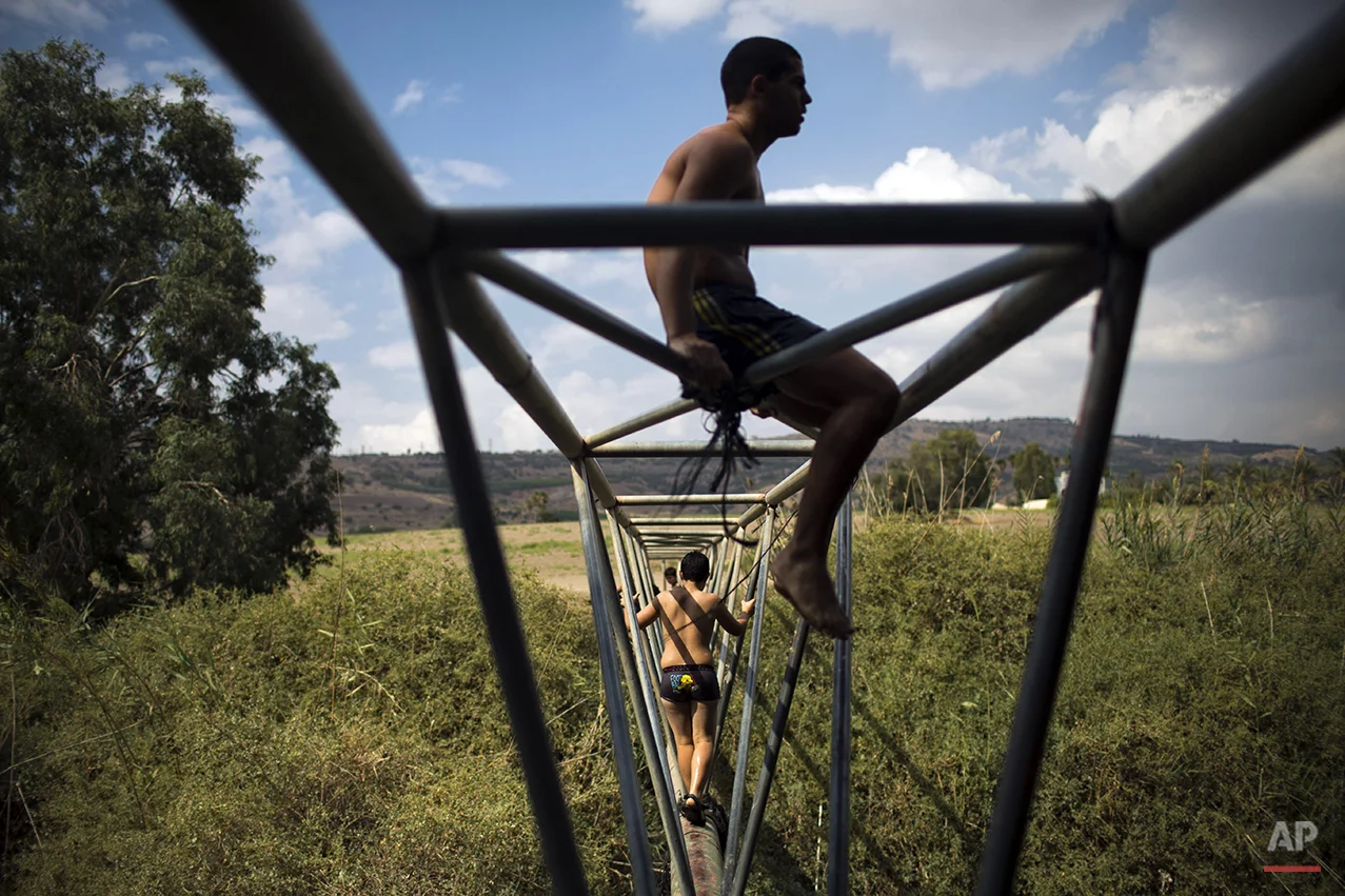 Israeli youth walk on a water pipe on the Jordan river during the week long Jewish holiday of Sukkot, near the northern Israeli town of Tiberias, Tuesday, Oct. 14, 2014. (AP Photo/Oded Balilty)