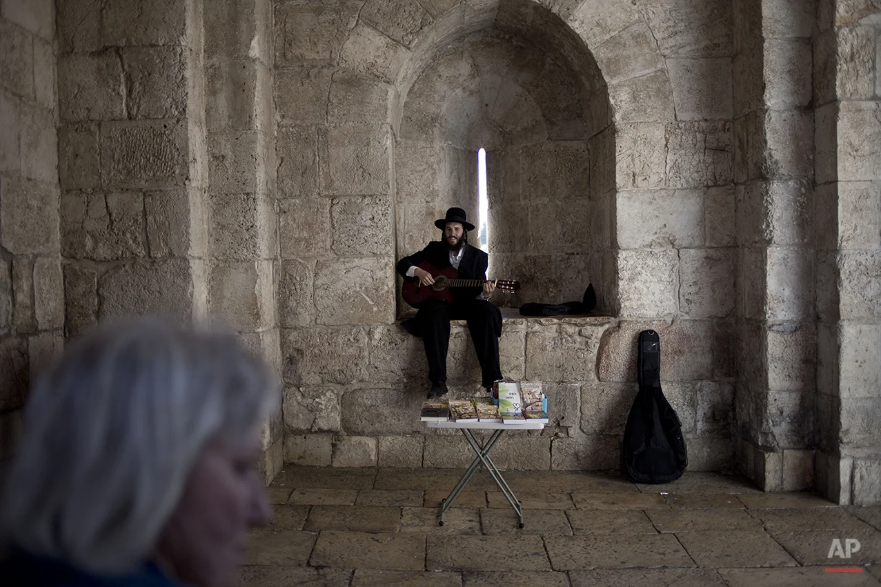 A Jewish Orthodox man plays the guitar as he sells religious books in Jerusalem's old city Jaffa Gate, Wednesday, April 30, 2014. (AP Photo/Ariel Schalit)